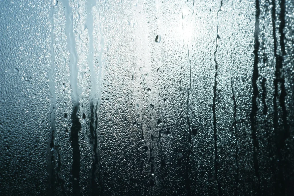 Close-up of glass covered in fine condensation droplets, with streaks where water has run down the pane.